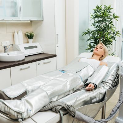 Blonde girl lying on beauty couch during pressotherapy session in clinic